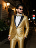 Man wearing a gold suit with black lapels on a city street at night.