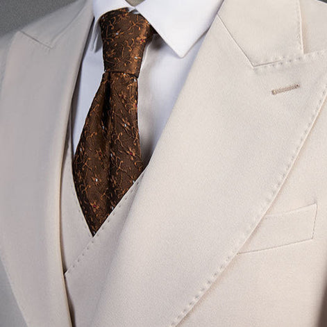 Close up of wide peak lapel and chocolate brown tie on beige suit jacket |
