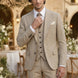 Man in a beige suit standing in an outdoor setting with tables and floral arrangements.