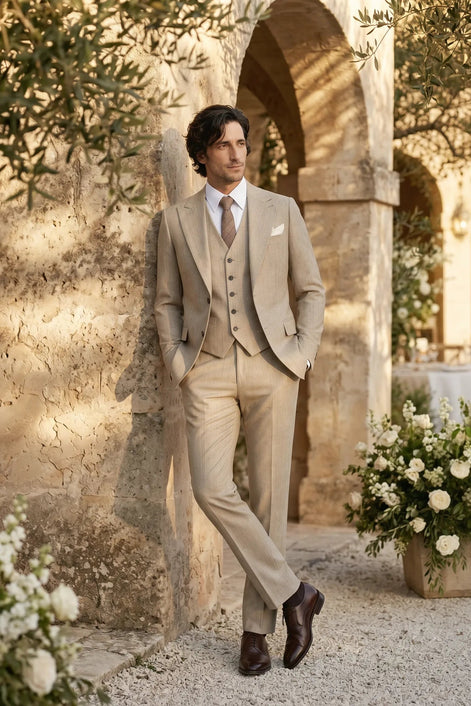 Man in a beige suit standing in an outdoor setting with floral arrangements and stone architecture.