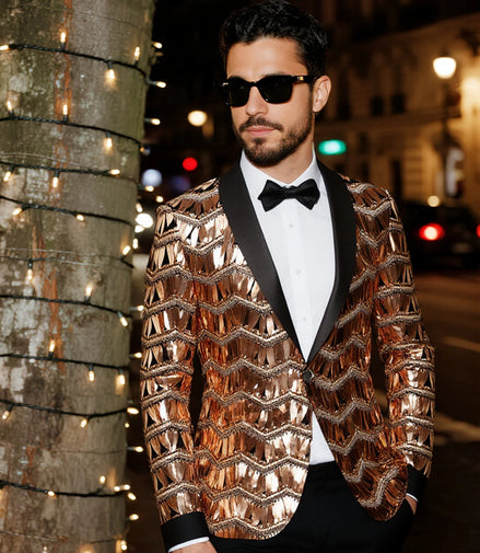 Man wearing a shiny gold jacket and black bow tie on a city street at night.