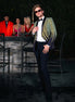 Man in a stylish outfit with a blurred background of people and a bar.