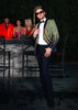 Man in a stylish outfit with a blurred background of people and a bar.