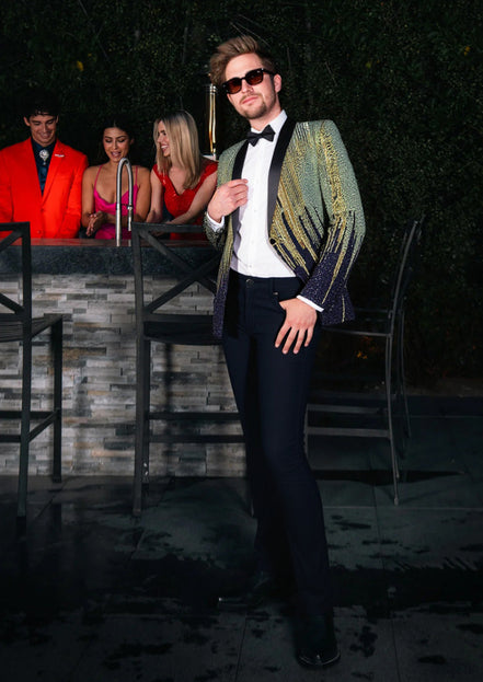 Man in a stylish outfit with a blurred background of people and a bar.