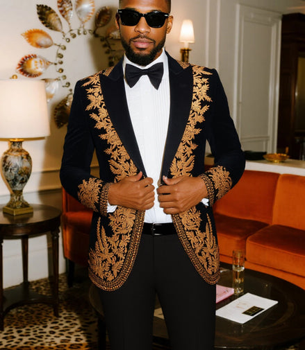 Man in a black and gold embroidered suit standing in an elegant room with orange sofa and decorative items.