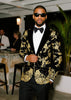 Man wearing a black tuxedo with gold embroidery in an indoor setting