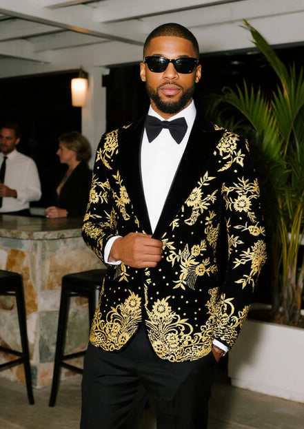 Man wearing a black tuxedo with gold embroidery in an indoor setting