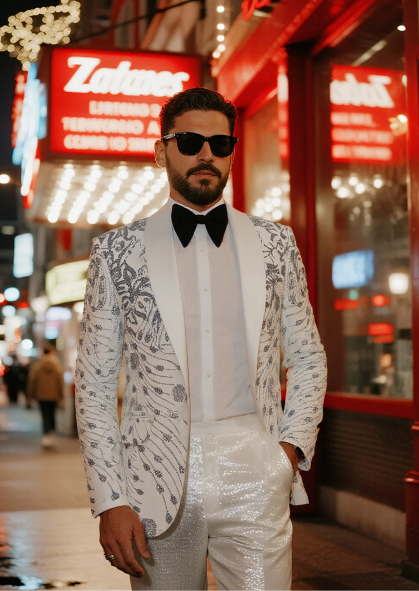 Man in a white patterned suit standing in front of a Zales jewelry store.